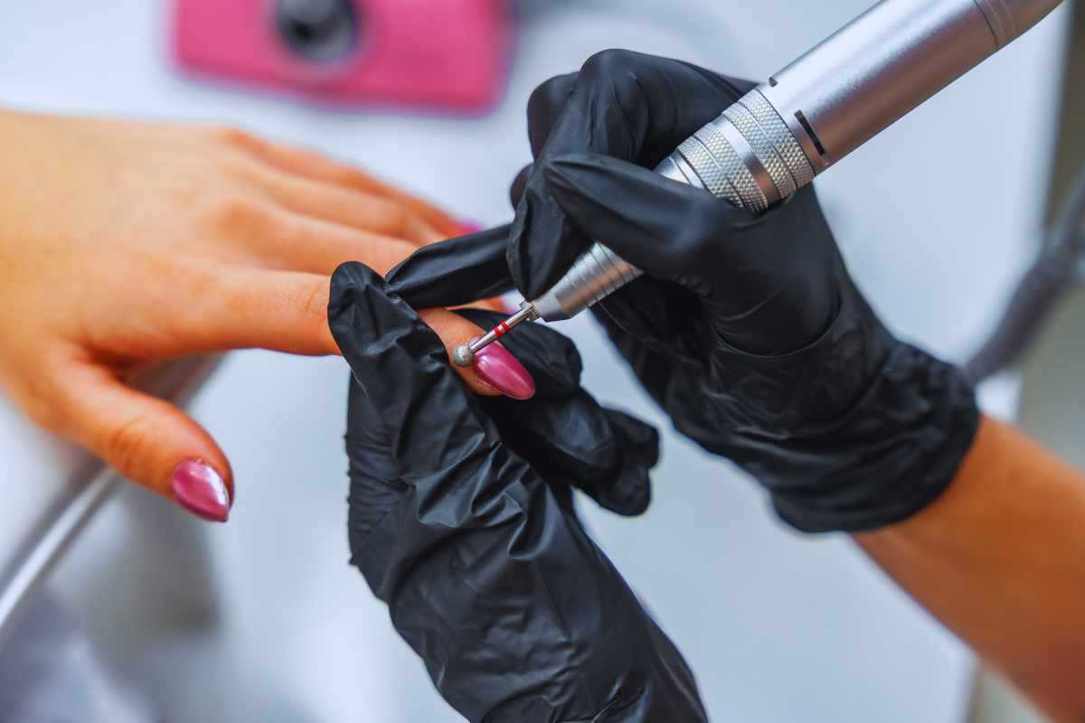 Mani con lo smalto che vengono lavorate da altri mani di un esperto estetista